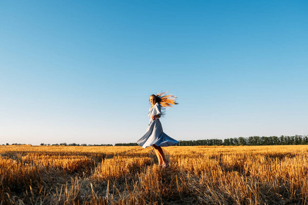 Escapism, getting away from it all, mental health, Stress resilience. Alone Young woman in linen dress walking on mowed wheat field at sunset. Peaceful woman with long hair spending time in nature