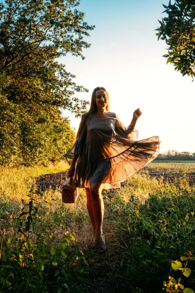 Cottagecore, simple living, slow life, country aesthetic lifestyle, modern rural fantasy, pastoral aesthetic. Young girl in peasant dress with straw handbag enjoying nature on sunset — Stock Photo, Image