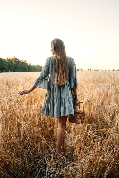 Cottagecore, einfaches Leben, langsames Leben, ländlicher Lebensstil, moderne ländliche Fantasie, pastorale Ästhetik. Junges Mädchen im Bauernkleid mit Strohhandtasche genießt die Natur bei Sonnenuntergang — Stockfoto