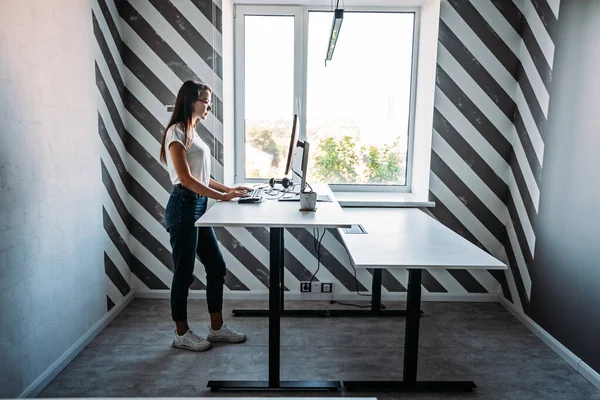 Standing Workplace. Working in Standing Position. Standing desk for work from home or in office. Young woman programmer working while standing in office — Stok fotoğraf