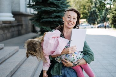 Serbest ebeveynler. Anne ve bebek kızıyla el üstünde yürüyüp sokakta tablete bakmakla meşguldüm. Bağımsız anne bebeğini kucağında tutarken notlar alıyor..