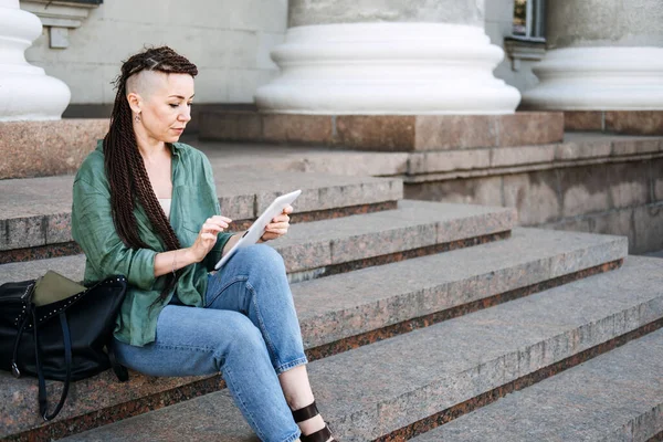 Fazladan para kazanmak, yan işler, para kazanmak, iş ekonomisi, dolandırıcılık, dijital göçebe. Fazladan para kazanmak için ek işler. Dışarıda çalışan dövmeli ve rastalı genç bir kadın.