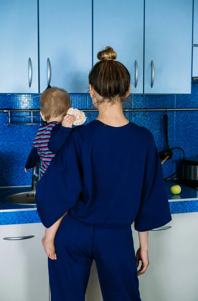 Young mother holding cute baby daughter in kitchen. Happy family mother and baby toddler girl cooking food at home kitchen. Household chores after the birth child — стоковое фото