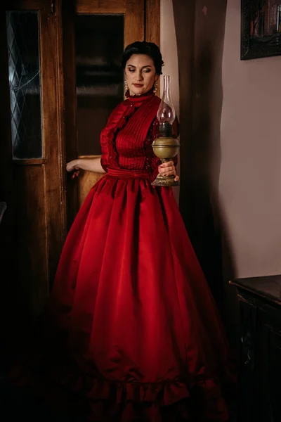 Beautiful woman in vintage 1800s early 1900s clothing red dress in old interior. Historical dresses, vintage outfits, beautiful retro dress reconstruction.