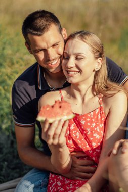 Yaz pikniğinde karpuz seven genç bir çift. Sevgili çift nehir kenarında oturuyor, konuşuyor, gülüyor, gülüyor, karpuz yiyor..