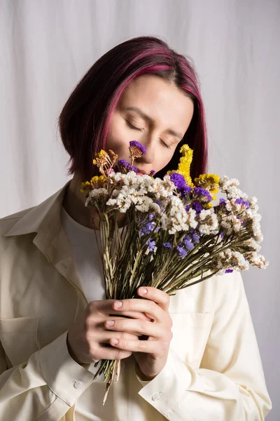 Candid portrait of young beautiful peaceful woman with purple hair with a bouquet of wildflowers. Natural light