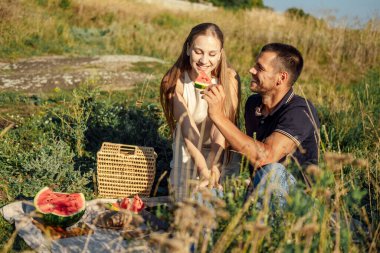 Romantik Piknik Randevusu Fikirleri. Yaz pikniğinde karpuz seven genç bir çift. Sevgili çift nehir kenarında oturuyor, konuşuyor, gülüyor, gülüyor, karpuz yiyor..