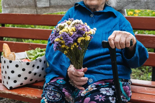 Holiday Gift Donations for Senior Citizens. Gift to help struggling seniors. Senior elderly woman with gift, flowers bouquet and basket of groceries sits on bench outdoor.