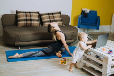 Ekstra Para Kazanmak İçin Fitness Side Hustles. Kişisel Antrenör Tarafı Koşuşturması. Genç anne fitness eğitmeni. Kişisel antrenör. Evde kızıyla birlikte dizüstü bilgisayarın yanında kişisel eğitim yapıyor.