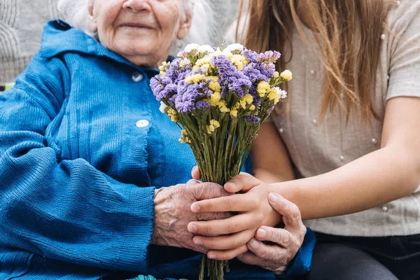 Holiday Gift Donations for Senior Citizens. Gift to help struggling seniors. Volunteer girl and Senior elderly woman with gift, flowers bouquet and basket of groceries