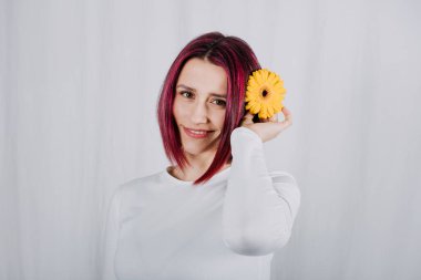 Stüdyo portresi, parlak kırmızı saçlı ve sarı çiçekli bin yıllık kadın. Renkli saç boyası. Saçına zarar vermeden yoğun bir renk.