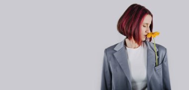 Gri ceketli, sarı çiçekli, parlak kırmızı saçlı, mutlu genç bir kadının samimi portresi. Stüdyoda, gündelik kıyafetli yeni yetme bir kızın fotoğrafı.