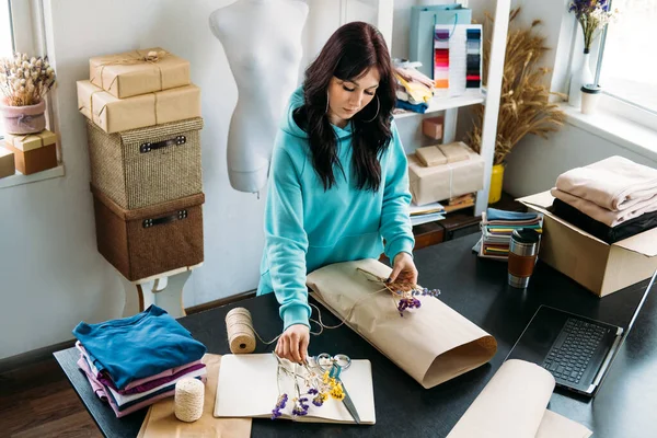 Small business owner woman packs the goods in eco packaging in office, shop. Female online store shop owner entrepreneur packing package box in eco friendly craft paper and cardboard