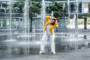 Kendine güveni tam, kıvrımlı, dans eden genç bir kadın modern arka planda. Binlerce yıllık neşeli, iri yarı bir kadın dışarıda eğleniyor ve dinleniyor. Vücut pozitifi, büyük beden özgüveni