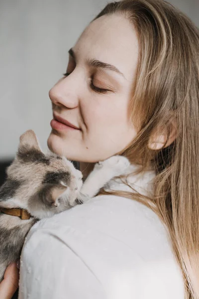 Cat Adoption, Adopt kitten from rescues and shelters. Portrait of woman playing with outbred homeless adopted grey kitten in bed at home