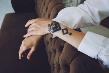 Female hands with tattoo on sofa at home. Relaxing woman tattoo hand close up