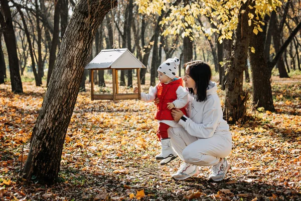 Family Fall Activities. Happy family mom and toddler baby girl feeding the birds outdoors in fall park. Little girl and her mother in the autumn park.