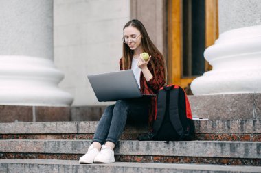 Student loan, Student finance for undergraduates. Outdoor portrait of happy student girl with laptop, papers and books near college, university