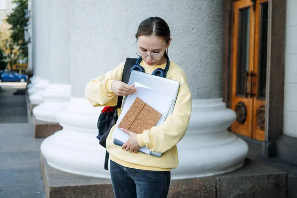 Student loan, Student finance for undergraduates. Outdoor portrait of happy student girl with laptop, papers and books near college, university