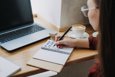 Main life goals, How to Set and Achieve Life Goals. Young woman girl writing in notebook the inscription My life goals while sitting with laptop and papers in cafe