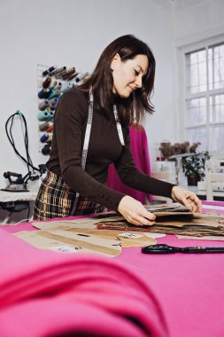Hand Cutting Pattern and Fabric Pieces. Fashion Design. Female tailor, seamstress working with sewing pattern on table in tailor shop, seamstress studio