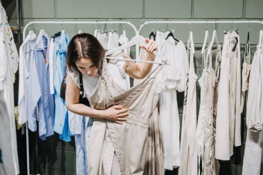 Sustainable fashion, slow fashion, Conscious shopping. Young Latina woman shopping in modern clothing store. Female customer choosing clothes in fashionable shop with sustainable designs brand