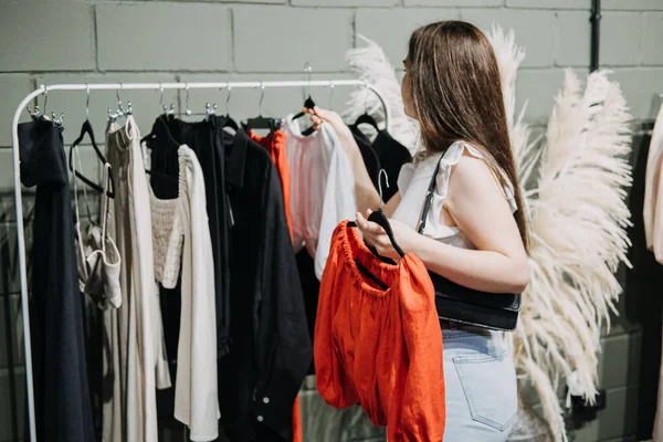 Sustainable fashion, slow fashion, Conscious shopping. Young Latina woman shopping in modern clothing store. Female customer choosing clothes in fashionable shop with sustainable designs brand