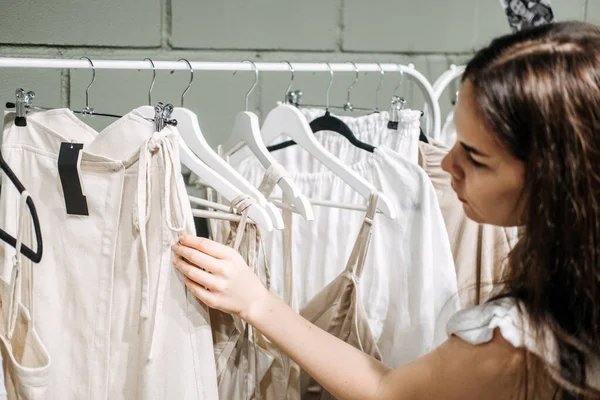 Sustainable fashion, slow fashion. Close Up Shot of female hand taking clothing rack with natural tones clothes made of 100 cotton linen organic materials.