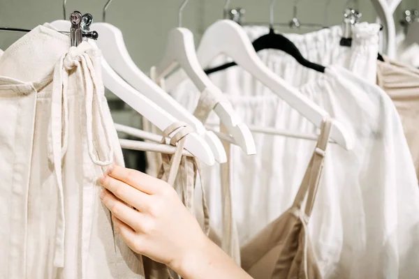 Sustainable fashion, slow fashion. Close Up Shot of female hand taking clothing rack with natural tones clothes made of 100 cotton linen organic materials.