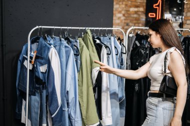 Modern Latina young woman choosing 100 percent organic cotton wear in modern eco-friendly showroom. Young Female Customer Shopping in Clothing Store