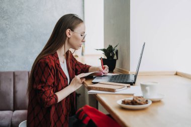 How to work more productively. Young woman student, freelancer working with laptop and documents in cafe, coworking workplace