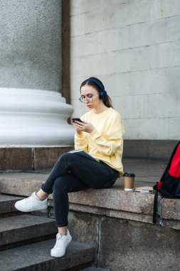 Study Tips for Back to School, Habits of Successful Students. Outdoor Portrait of student girl with headphones, books and notebook preparing for lesson, reading lecture summary