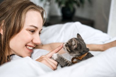 Cat Adoption, Adopt kitten from rescues and shelters. Rehome a Cat. Portrait of woman playing with two outbred homeless adopted grey kittens in bed at home
