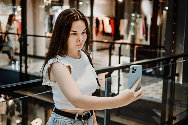 Young Latina woman with shopping bags using her smart phone while standing in shopping center, mall. Woman In Shopping Mall Using Mobile Phone