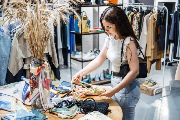 Sustainable fashion. Modern Latina young woman choosing handmade knitted handbag, recycling accessories in eco-friendly shop showroom, shop in shopping mall