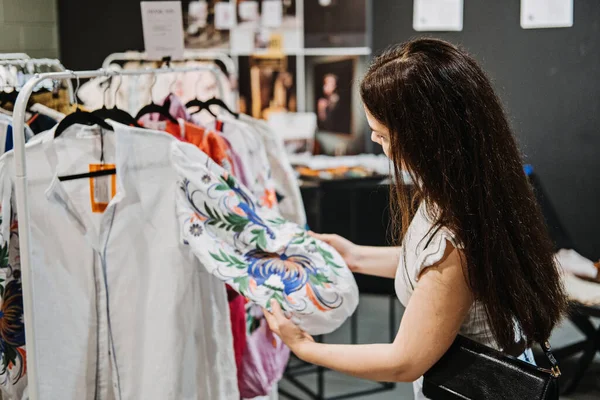 Sustainable fashion. Young latina young woman choosing boho ethnic clothing in vintage shop in shopping mall