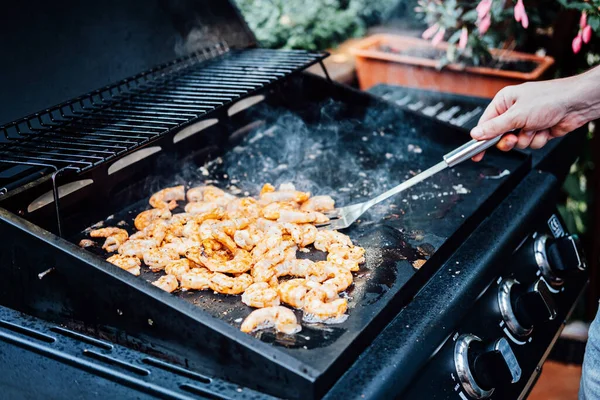 Grilling shrimp on skewer on outdoor grill. Grilled shrimps on the flaming grill. Man hand using tong pinching grilled seafood on smoked barbeque grill roaster