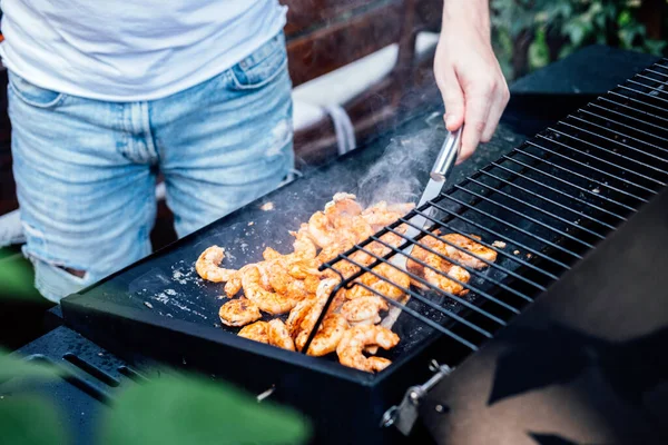 Grilling shrimp on skewer on outdoor grill. Grilled shrimps on the flaming grill. Man hand using tong pinching grilled seafood on smoked barbeque grill roaster