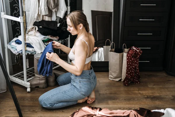 Organize closet, decluttering wardrobe. Young woman decluttering wardrobe and choosing clothes in her bedroom