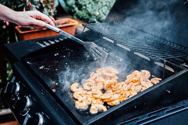 Grilling shrimp on skewer on outdoor grill. Grilled shrimps on the flaming grill. Man hand using tong pinching grilled seafood on smoked barbeque grill roaster