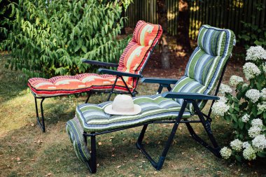 Two soft sun loungers with straw hat in inner courtyard. Two empty sun beds in a sunny garden for relaxation. Work life balance