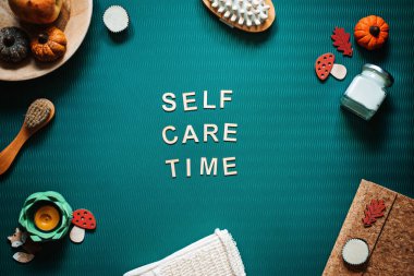 Self-care time word on green background flat lay. Self-care time text wooden letters with body face care products and autumn decor. Take care of yourself in autumn, winter cold season