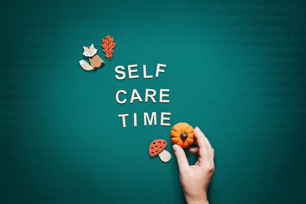 Self-care time word on green background flat lay. Self-care time text wooden letters with body face care products and autumn decor. Take care of yourself in autumn, winter cold season