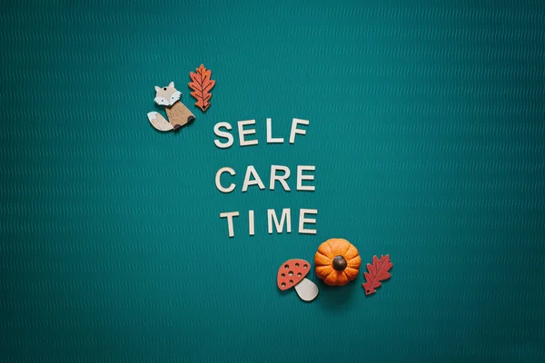 Self-care word on green background flat lay. Self-care text wooden letters with body face care products and autumn decor. Take care of yourself in autumn, winter cold season
