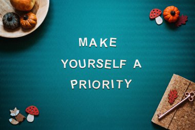 Self-care quotes, make yourself a priority words on green background flat lay. Self-care text wooden letters with autumn decor. Take care of yourself in autumn, winter cold season