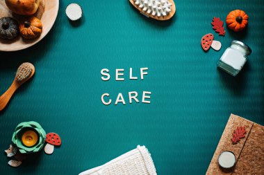 Self-care word on green background flat lay. Self-care text wooden letters with body face care products and autumn decor. Take care of yourself in autumn, winter cold season