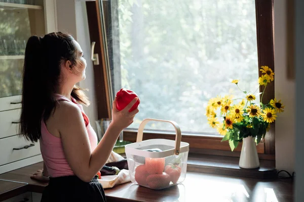 Vegan food and health. Vegans Eat. Young Latina woman holding red Bell pepper near vegetables on table in home kitchen
