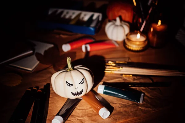 Halloween arts and crafts. Painting pumpkins, brushes and paints on the table on dark night. Close up of painted pumpkin for Halloween