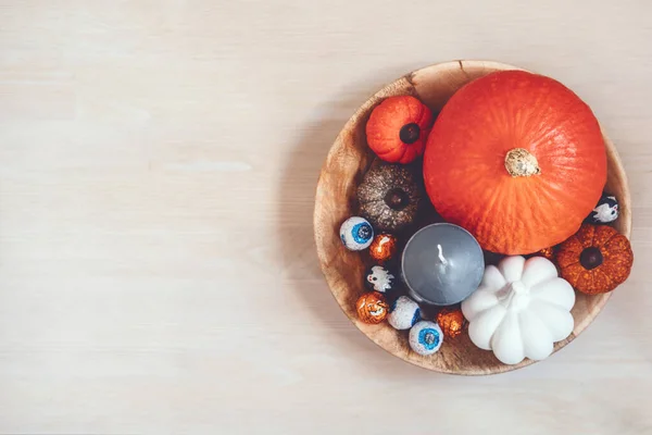 Minimal Halloween holiday decoration with pumpkins, candies, black candles on wooden table. Indoors Sustainable Eco-Friendly Halloween holiday decoration.