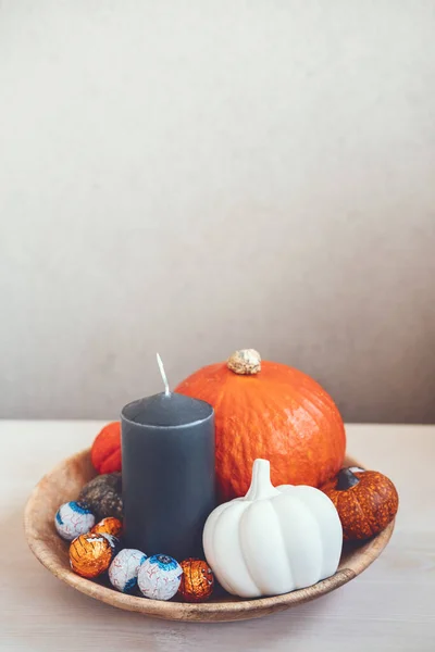 Minimal Halloween holiday decoration with pumpkins, candies, black candles on wooden table. Indoors Sustainable Eco-Friendly Halloween holiday decoration.